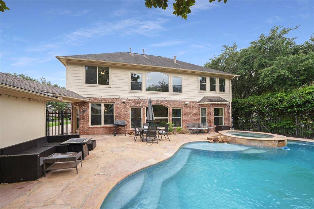 This spacious backyard features a two-story brick and siding home with a large patio, perfect for entertaining. It includes a swimming pool and a spa, surrounded by lush greenery for privacy.