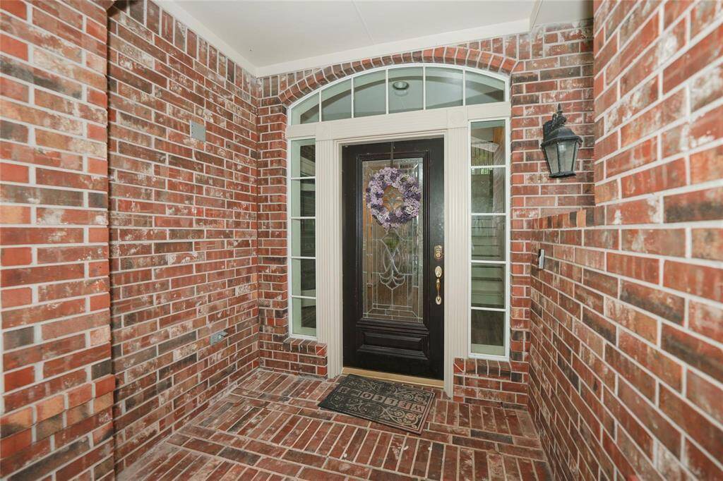 Inviting brick entryway featuring a decorative black door with sidelights and an arched transom window. A charming wreath adds a welcoming touch, and a wall-mounted lantern provides lighting.