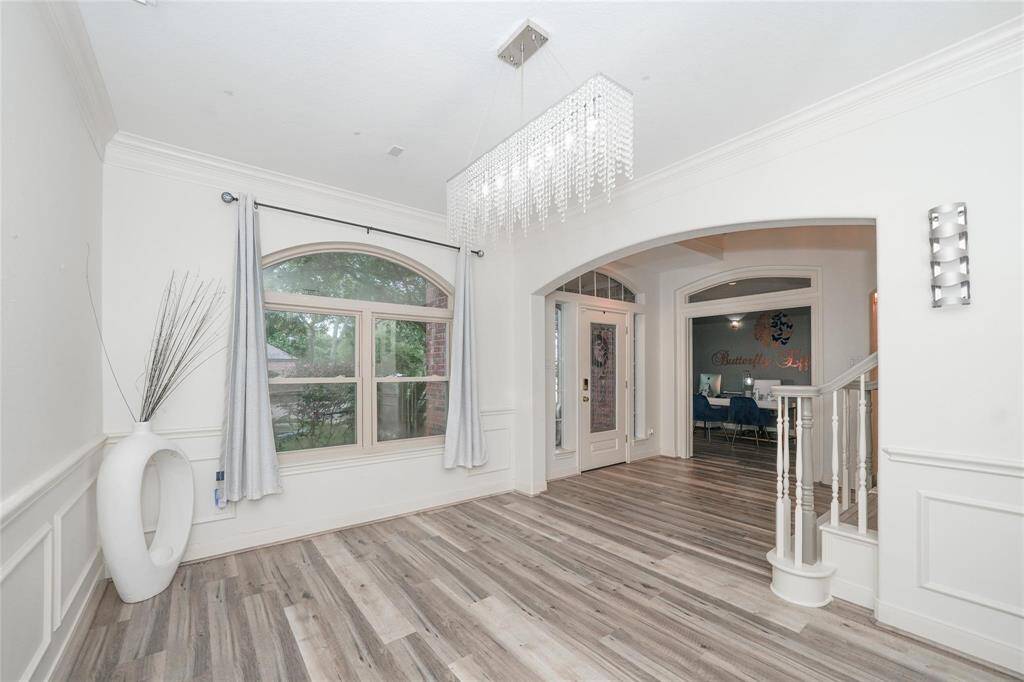 Bright and spacious entryway with modern wood flooring, large arched window, elegant chandelier, and decorative molding, leading to a welcoming interior space.