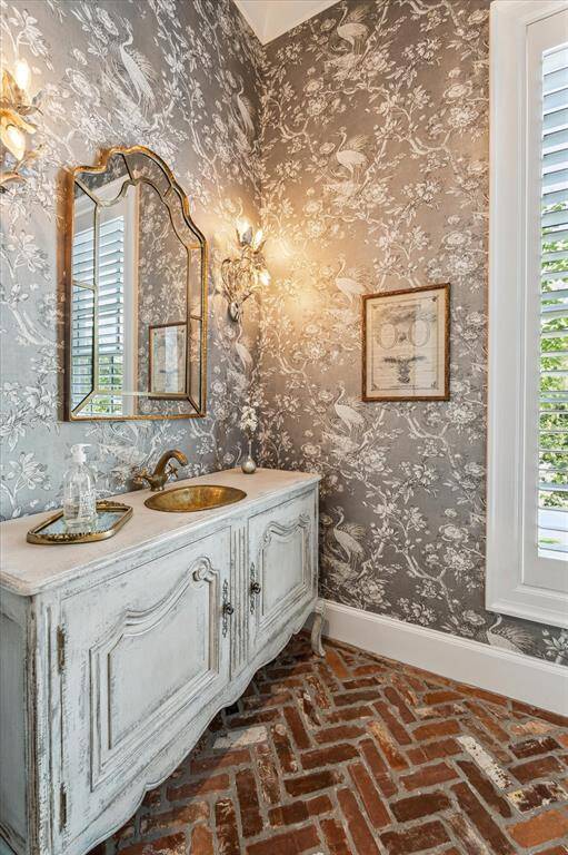 Sublime powder room includes custom vanity with handmade brass basin & faucet, elegant wallpaper & herringbone patterned reclaimed brick flooring.
