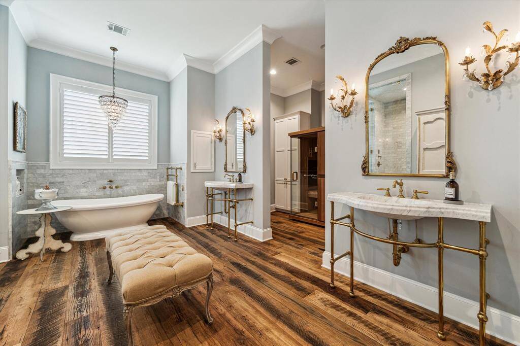 Stunning Primary Bath exudes French Country style, boasting dual vanities created with sinks carved into single slab of Carrera marble. Brass fixtures, imported English brass towel warmer, opulent mirrors & lovely sconces create a supremely elegant space.