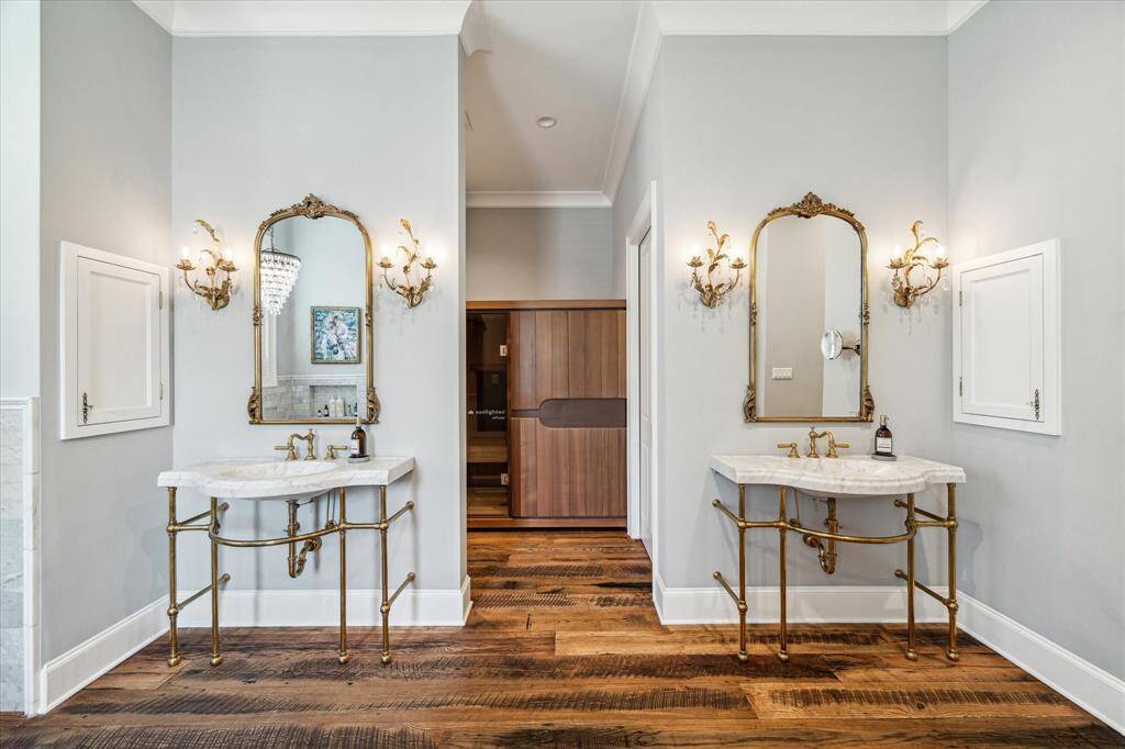 Beautiful view of custom vanities with built-in storage tucked away to the side. Luxurious sauna is just behind, and note the beautiful antique wood flooring.
