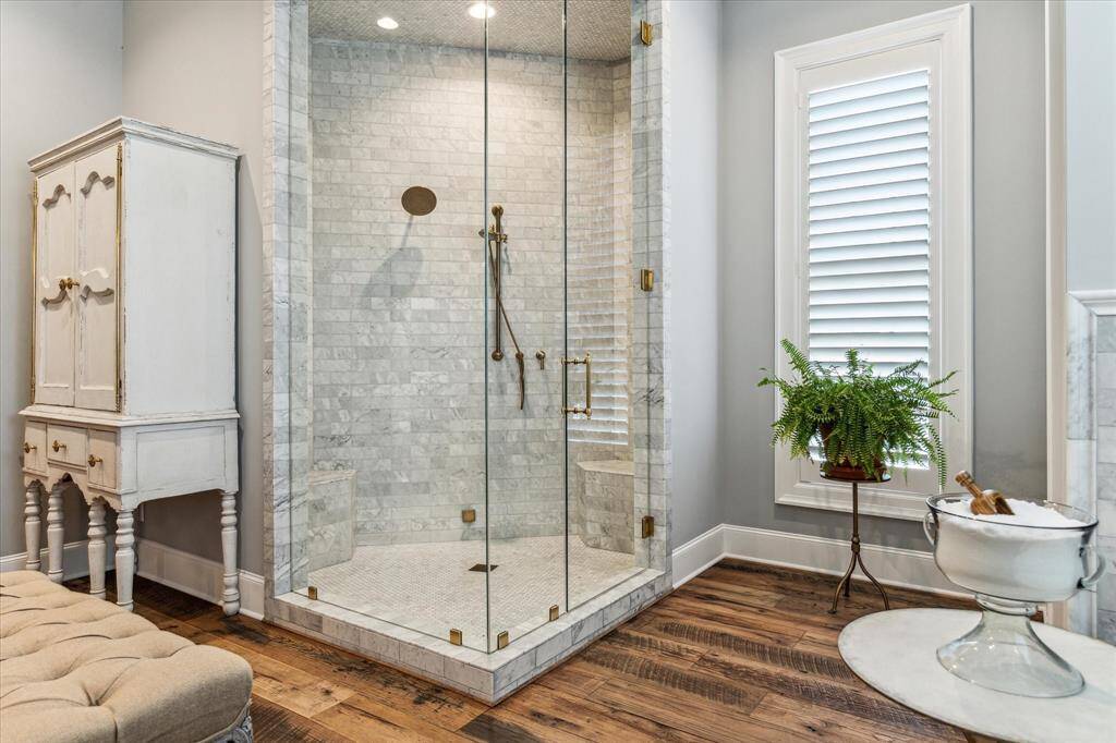 Closer view of glass enclosed shower featuring intricate marble tile surround & brass hardware.