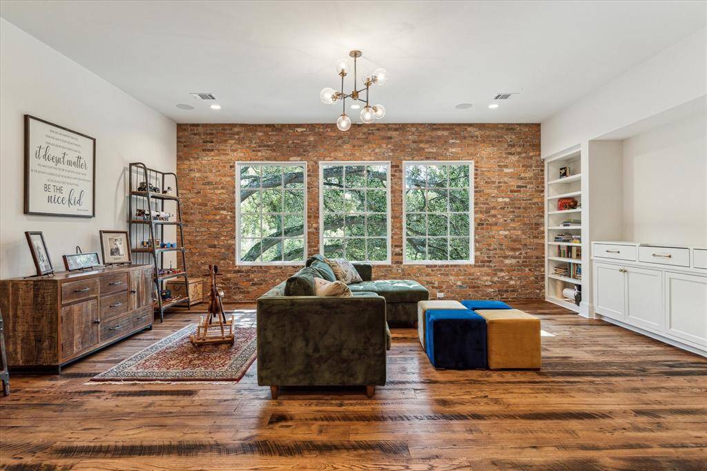 Second floor game room features antique hardwood floors, accent walls fashioned from reclaimed brick, abundant windows offering treetop views & custom cabinetry/built-ins.