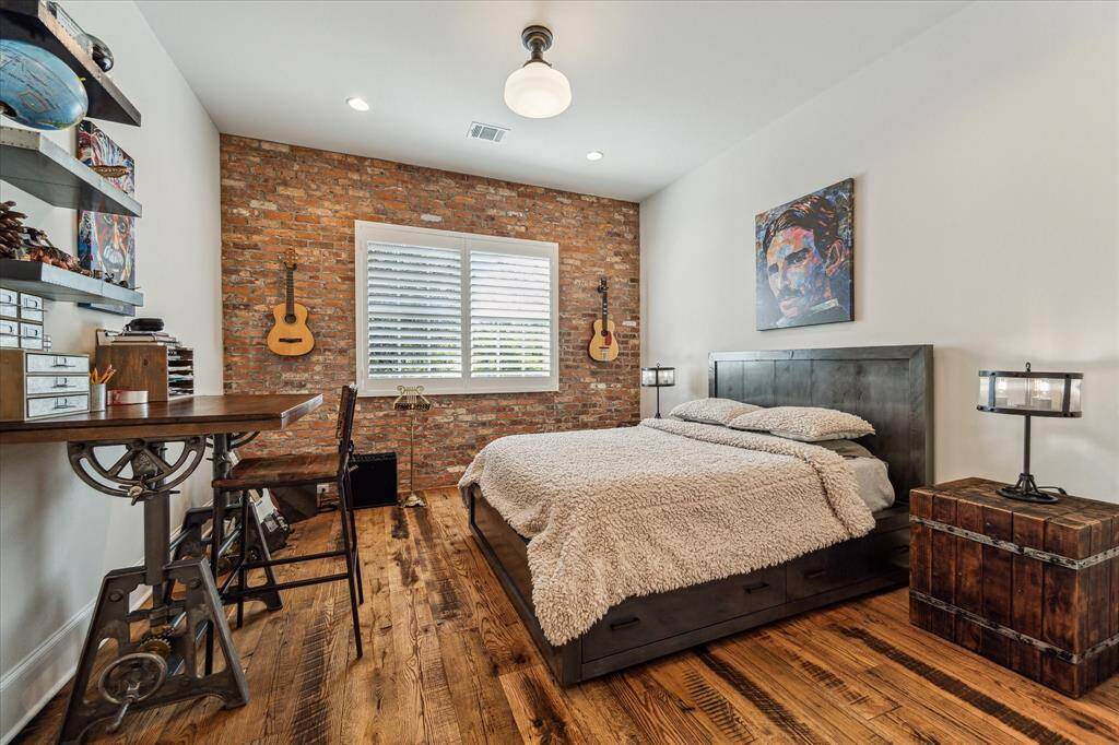 One of four spacious secondary bedrooms, all with reclaimed brick accent walls, antique hardwood floors & well-appointed en suite baths.