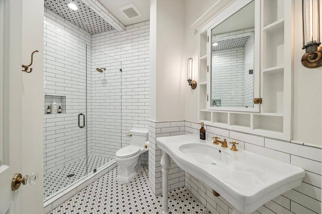 One of four beautifully appointed secondary bathrooms, all en suite. Each bath features ceramic vanity with integrated sinks, custom medicine cabinets with mirrors & extra storage, oversize glass enclosed showers sized to fit tub, plus hexagon & subway tile surrounds that extend to ceiling.