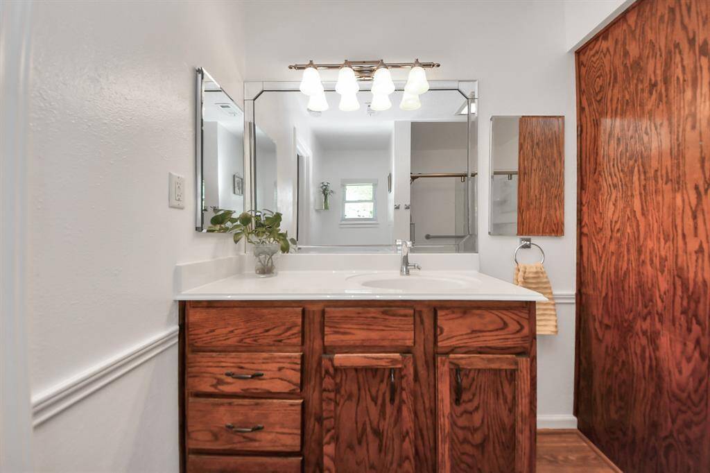 Light and bright, featuring a large mirror with elegant lighting, a spacious countertop with wooden cabinetry.