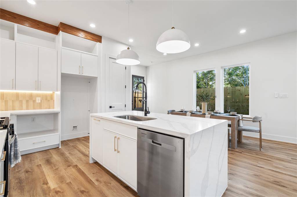 The kitchen is illuminated by dome pendant lighting over the island and undermounted LED ceiling lights, enhancing the bright and airy feel.