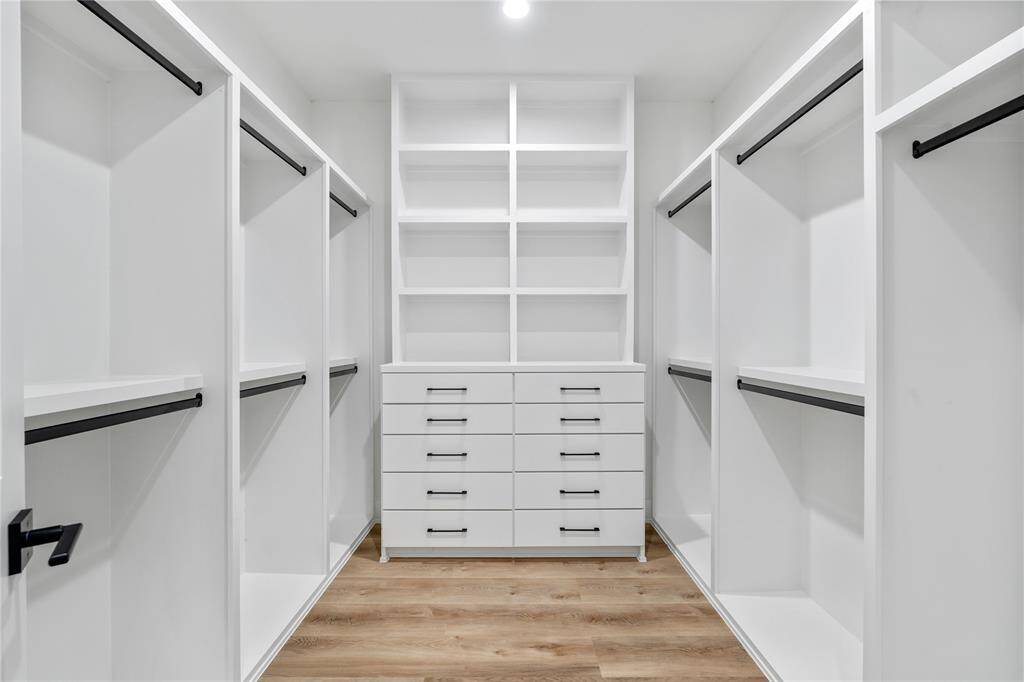 A luxurious walk-in primary closet, designed for maximum organization and style. This expansive space offers a blend of custom-built storage solutions and a sleek, modern design to keep everything effortlessly organized.