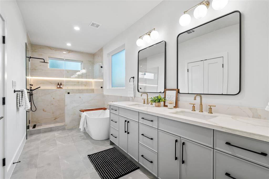 A breathtaking spa-like en-suite bath featuring quartz countertops, dual sinks, a freestanding soaking tub, and a glass-enclosed walk-in shower with designer tile.