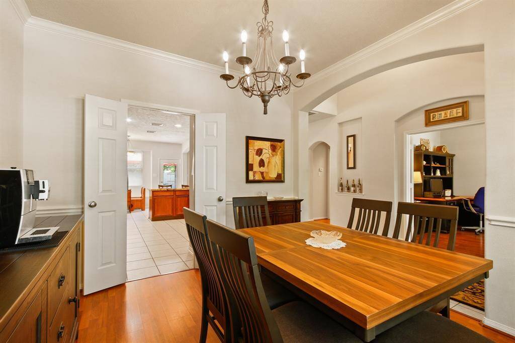 This photo showcases a warm, inviting dining area and a classic looking chandelier. The space features elegant archways, leading to a bright kitchen.