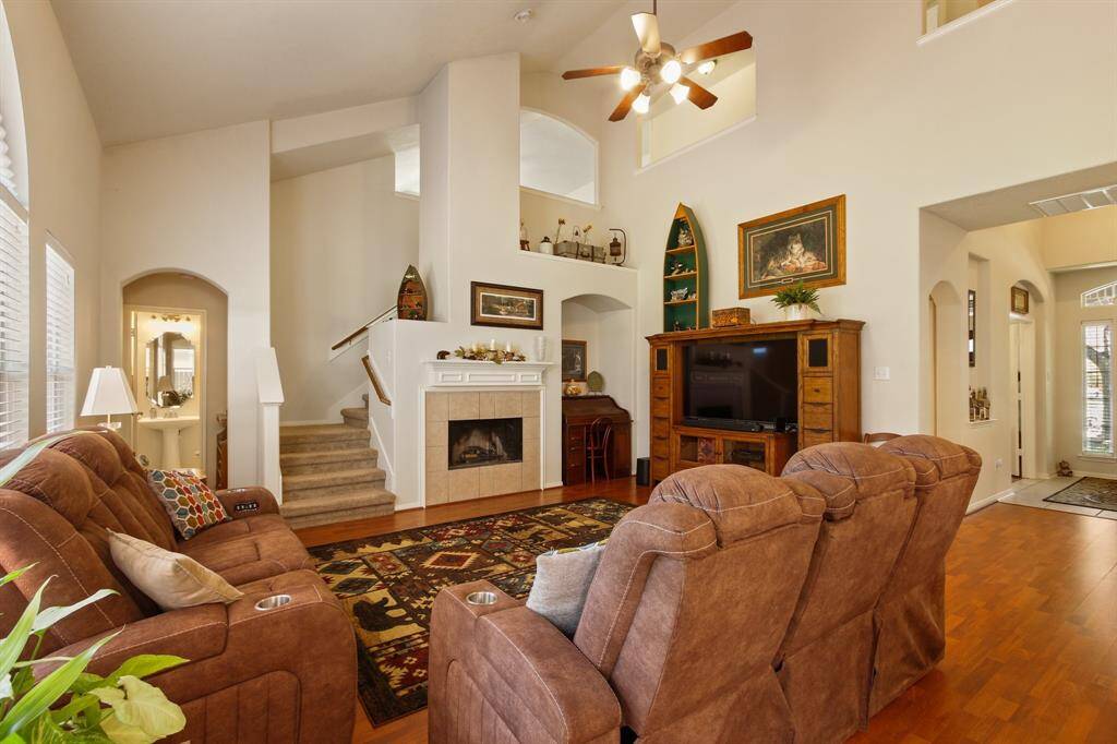 This inviting living room features high ceilings, a cozy fireplace, and ample natural light. It includes, and an open staircase, creating a warm and spacious atmosphere perfect for relaxation and entertaining.