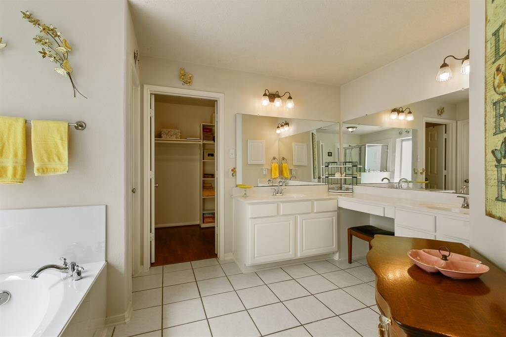 This bathroom features a spacious layout with dual sinks, a large mirror, and bright lighting. It includes a bathtub, tile flooring, and access to a walk-in closet, providing ample storage and convenience.