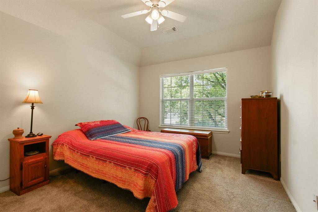 This cozy bedroom features a large window allowing natural light, neutral walls, and carpeted flooring. It includes a ceiling fan, and can easily accommodate a good size bed, set of drawers and a side table.
