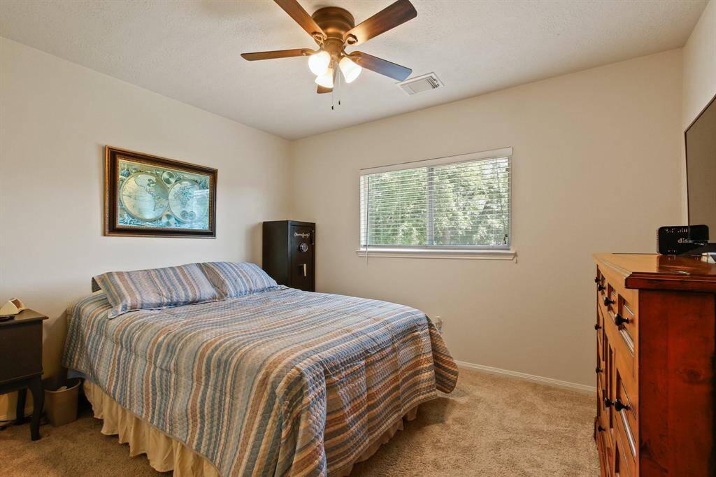 This extra bedroom features a ceiling fan, large window for natural light, neutral carpeting, all creating a comfortable and inviting space.