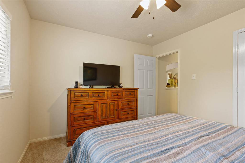 Cozy bedroom with neutral walls and carpet, featuring a ceiling fan and natural light from a window.