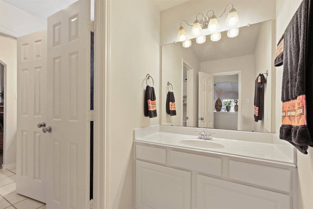 Bright bathroom with a large mirror, modern lighting, and a clean white vanity. Ample storage with double doors and elegant decor accents.