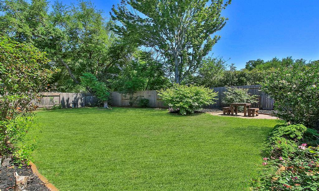 Spacious, well-maintained backyard with lush green lawn, mature trees, and a cozy patio area featuring a wooden picnic table.