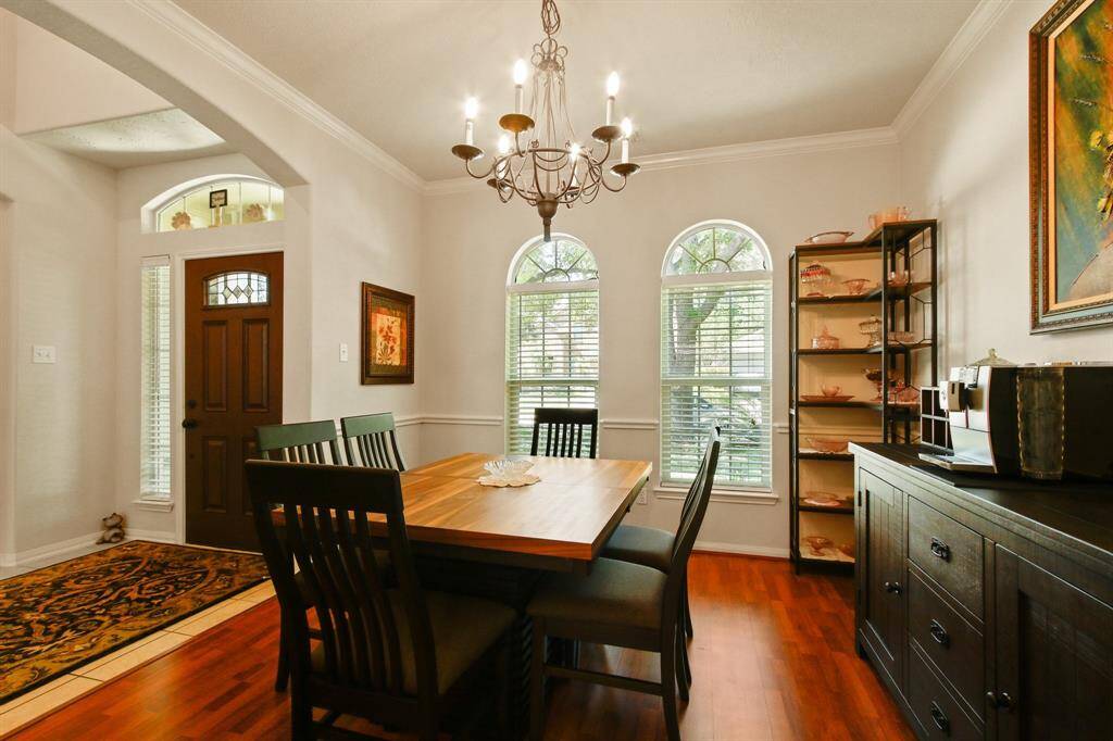 This dining room features elegant wood laminate flooring and a warm, inviting atmosphere. It shows a wooden dining table with matching chairs (used for staging), a stylish chandelier, and large arched windows that provide ample natural light. The space is accented with tasteful decor and offers a welcoming entryway.