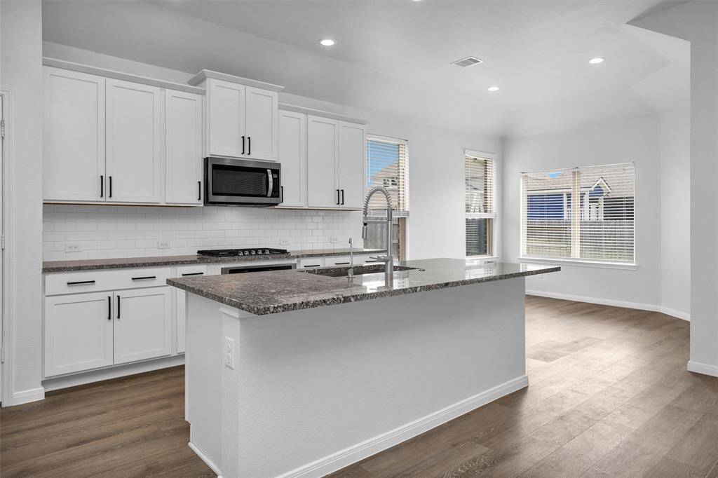 Beautifully appointed kitchen featuring white shaker cabinets, granite countertops, subway tile backsplash, and stainless steel appliances. A large island provides additional prep space and bar seating—ideal for casual meals and conversation.