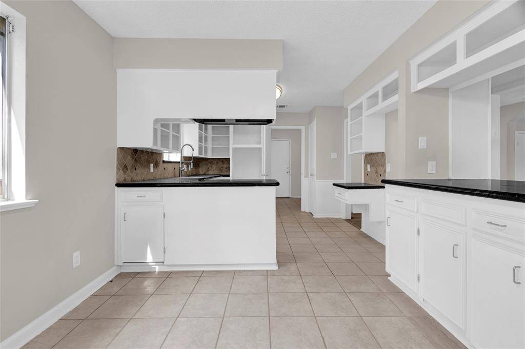 A clean, bright kitchen with a neutral color palette features white cabinetry, giving the space a fresh and airy feel, while black granite countertops add contrast and elegance.
