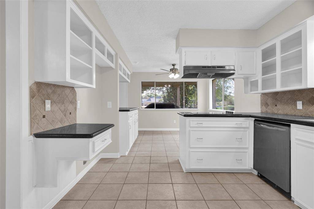 To the left is a built-in desk or workstation beneath open shelving, perfect for a kitchen command center or a laptop setup. The kitchen opens up to a breakfast nook, illuminated by large windows that let in lots of natural light and provide a nice view of the backyard.