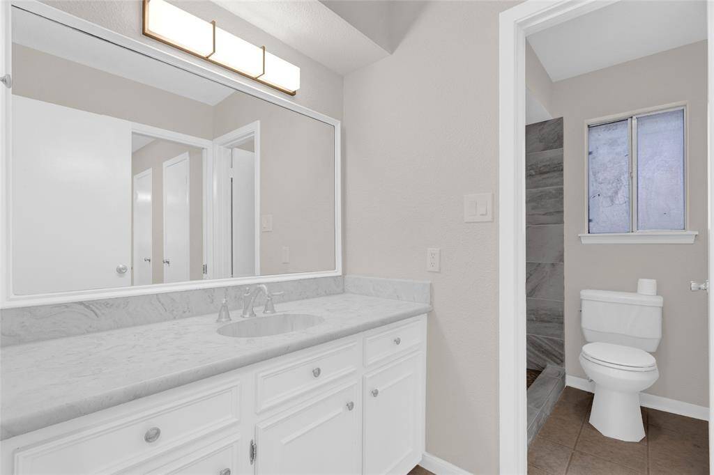 This beautifully updated bathroom features a sleek marble-look vanity with ample counter space and storage. The expansive mirror and modern lighting add a touch of elegance, while the separate toilet and walk-in shower area provide both privacy and functionality.