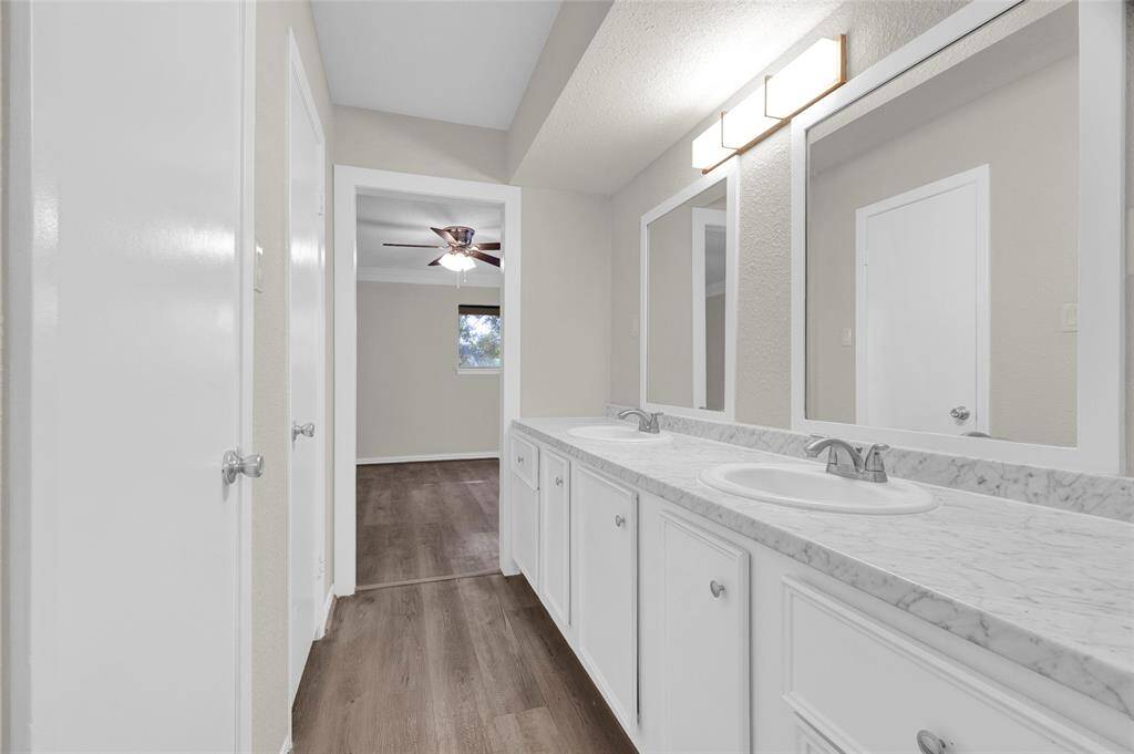 Retreat to this elegant master bathroom featuring a dual-sink vanity with marble-look countertops and ample cabinet storage. Two oversized mirrors and sleek modern lighting offer a bright, spa-like feel.