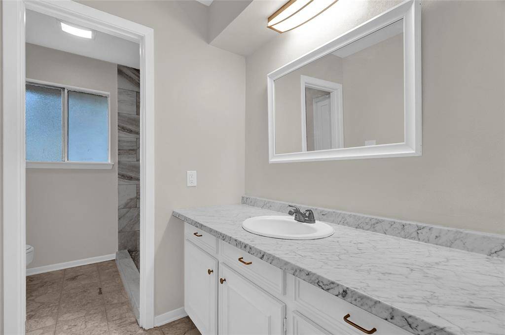 This updated secondary bathroom features a sleek marble-look countertop, modern lighting, and ample vanity storage.