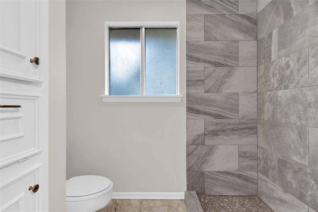 The walk-in shower showcases stylish gray tile with striking natural veining, complemented by a pebble stone shower floor for added texture and spa-like comfort.  Please note the wall of built-ins on the left!
