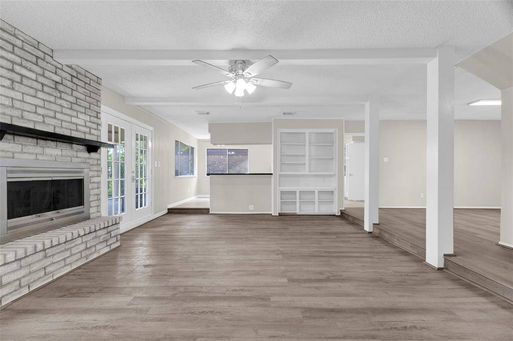 Here’s another view of the spacious living area, emphasizing its open layout and seamless flow between rooms. The large brick fireplace anchors the space with a cozy, rustic charm, while double French doors invite natural light and frame views of the future golf course just beyond the backyard.