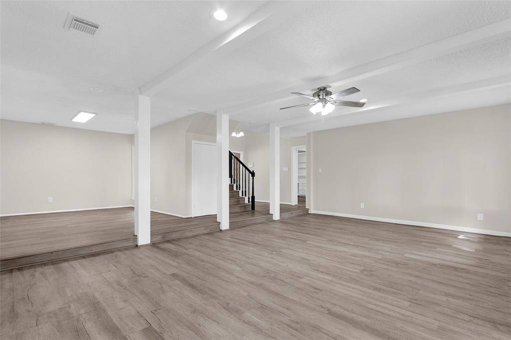 The flooring throughout is a light wood-style vinyl plank, adding a modern yet warm touch. Multiple white support columns divide the space subtly without closing it off, creating distinct zones while maintaining an open flow.