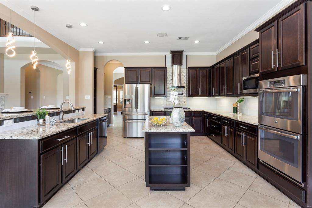 Spacious kitchen with modern dark wood cabinetry, granite countertops, and stainless steel appliances. Features a central island, double ovens, and stylish pendant lighting, offering a perfect blend of functionality and elegance.