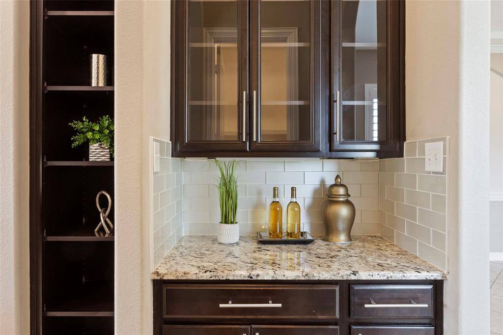 Off of the kitchen is a stylish bar or coffee bar area with dark wood cabinets, glass doors, and a granite countertop.