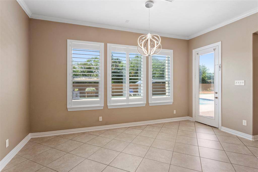 Large breakfast dining area with tiled floors, large windows with plantation shutters, and a modern light fixture. A glass door leads to a patio with a pool view, offering ample natural light and outdoor access.