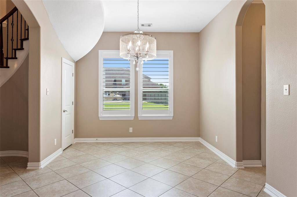 Beautiful formal dining area with tiled flooring, neutral walls, and an updated chandelier. Features large windows with plantation shutters, providing ample natural light. Arched doorways add architectural interest.