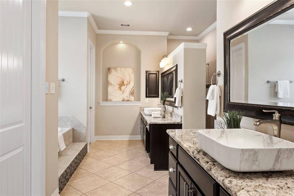 This elegant ensuite Primary Bathroom features a spacious layout with dual granite-topped vanities, a large mirror, and a vessel sink. The tile flooring complements the neutral tones, while recessed lighting adds warmth.