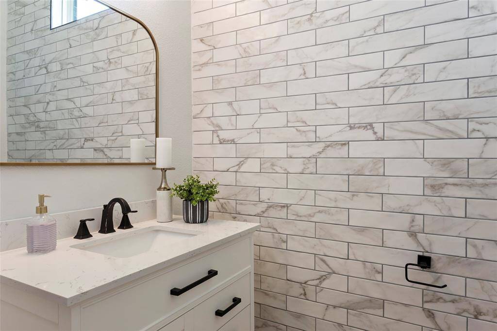 The downstairs guest bath features a sleek, modern design with a marble-tiled wall, a white vanity with black fixtures, and a large mirror. The space is bright and inviting, perfect for a contemporary home.