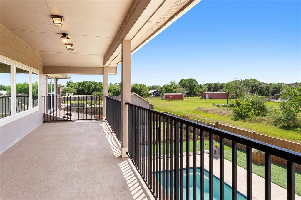 Large, covered balcony with modern lighting, offering a scenic view of a lush green backyard and a pool, perfect for relaxation and outdoor enjoyment.