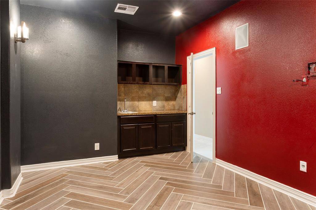 The dedicated Media Room features a true theater color scheme, with herringbone-patterned tile flooring. It includes a wet bar with dark wood cabinets and a small sink. Recessed lighting and dimming wall sconces provide illumination.