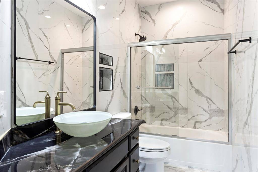 Elegant upstairs bathroom featuring a modern vessel sink on a sleek black marble countertop. It includes a bathtub with a glass sliding door and striking marble-patterned walls for a luxurious feel.