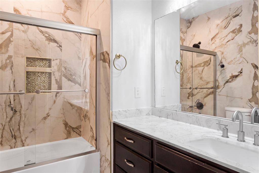 This upstairs bathroom features a modern design with marble-patterned tiles, a glass-enclosed shower, and a sleek vanity with a large mirror.