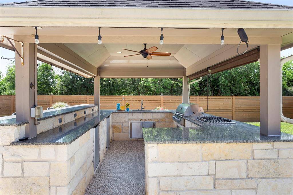 The custom outdoor kitchen is covered and features a built-in grill, sink range stovetop, refrigerator, ample counter space with granite tops, and ceiling fans. It's perfect for entertaining!