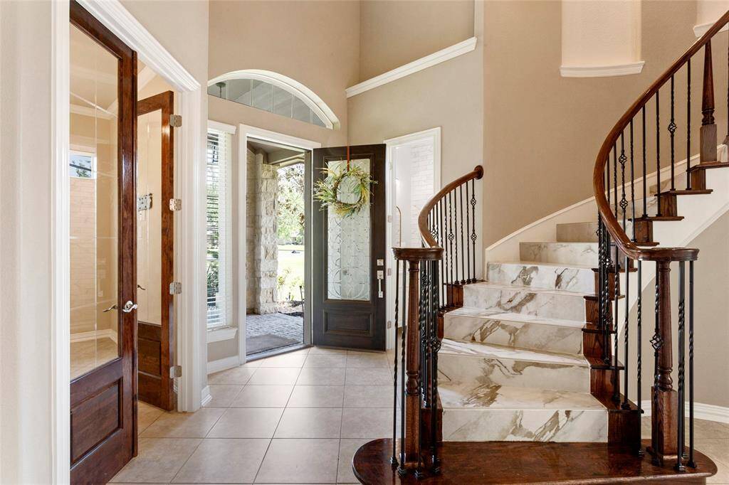 This dramatic entryway features a stylish curved staircase with marble steps and elegant wrought iron railings. The space is well-lit with natural light from large windows creating a striking first impression.