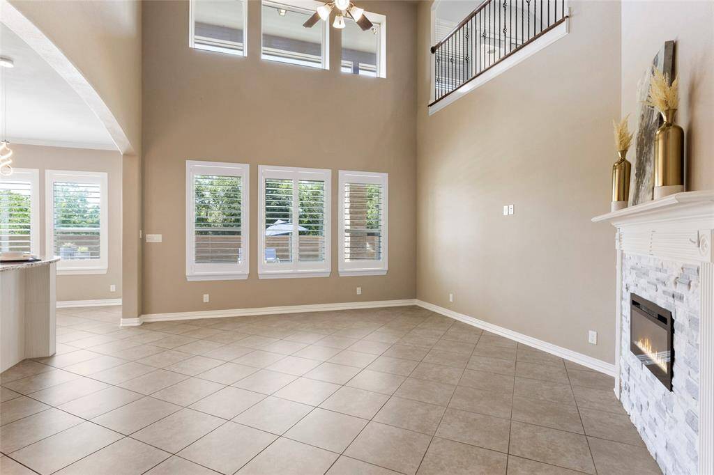 The living room features soaring ceilings, large windows with plenty of natural light, and an updated remote fireplace. The open layout includes a view of the upstairs balcony, and the tile flooring adds a sleek touch. Ideal for comfortable living and entertaining.