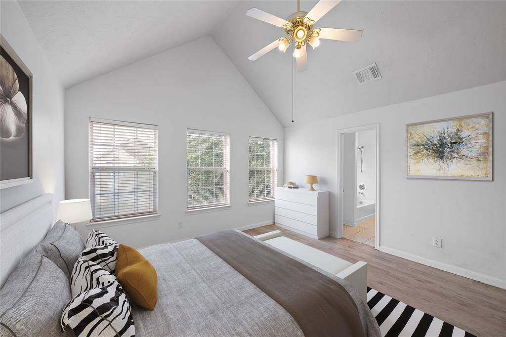 This bright primary bedroom features a high vaulted ceiling with a ceiling fan, three large windows for gorgeous natural light, and a large en-suite bathroom. It includes neutral colors, and wood flooring for a contemporary feel. The primary suite includes TWO CLOSETS!