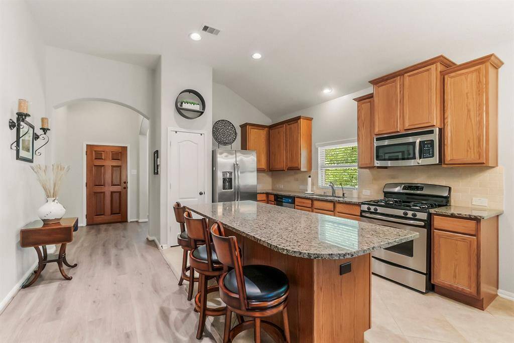 This kitchen features a spacious layout with a large island and seating. It includes stainless steel appliances, warm wood cabinetry, and ample natural light.