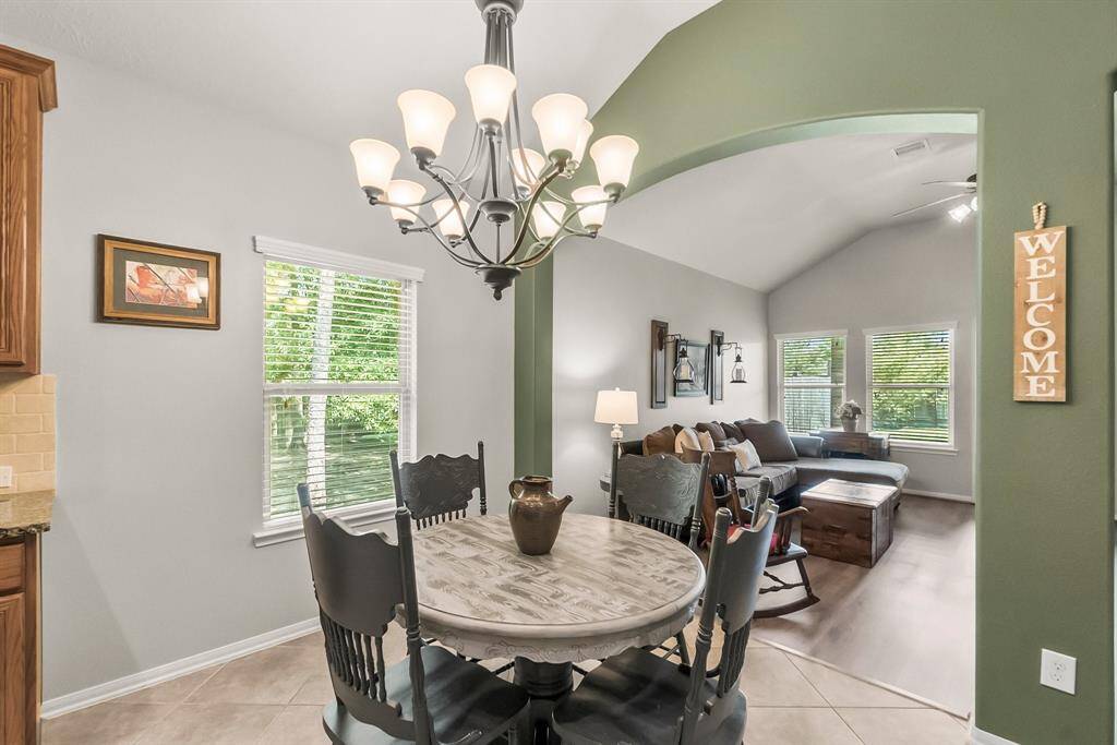 Bright and inviting open-concept space featuring a cozy dining area with a stylish chandelier, transitioning into a comfortable living room with large windows and a welcoming atmosphere.