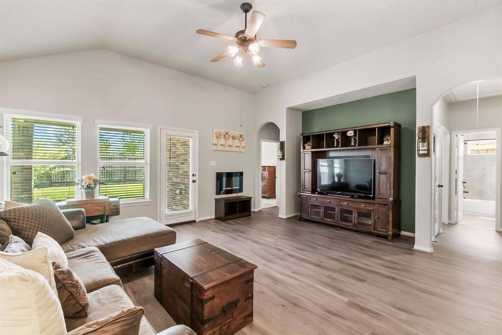 This spacious living room features high ceilings, large windows for natural light, and a ceiling fan with access to backyard.
