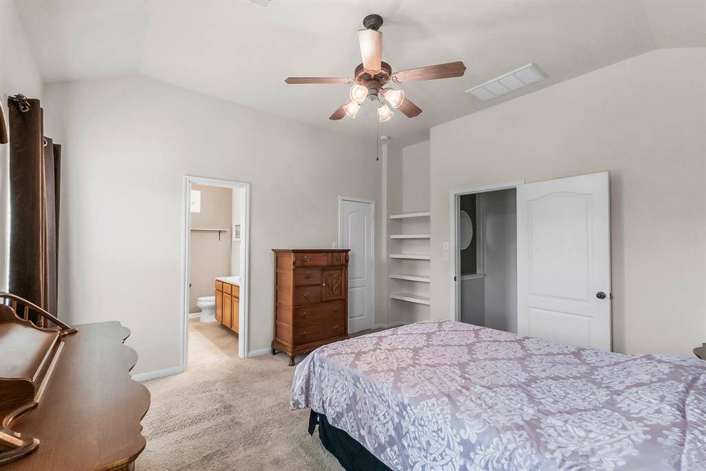 Primary bedroom features neutral walls, a ceiling fan, and carpeted flooring. It includes a connected bathroom, built-in shelves, and ample natural light.